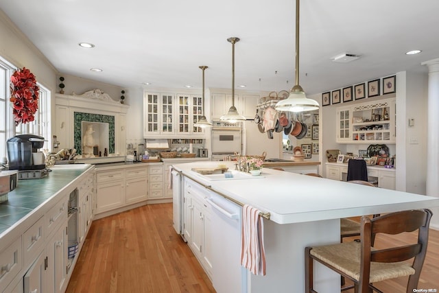 kitchen featuring pendant lighting, a breakfast bar, white appliances, light wood-type flooring, and a kitchen island with sink