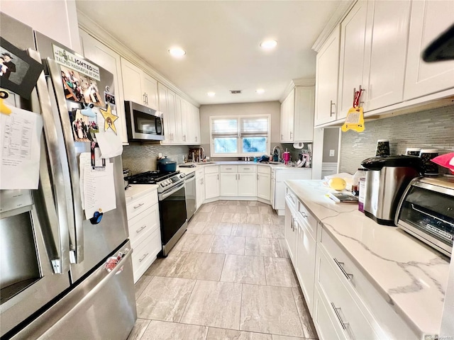 kitchen featuring decorative backsplash, light stone counters, white cabinets, and appliances with stainless steel finishes