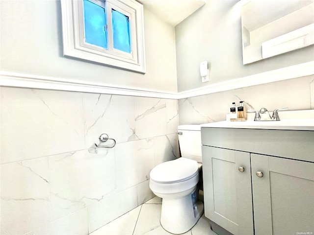 bathroom featuring tile patterned flooring, vanity, toilet, and tile walls