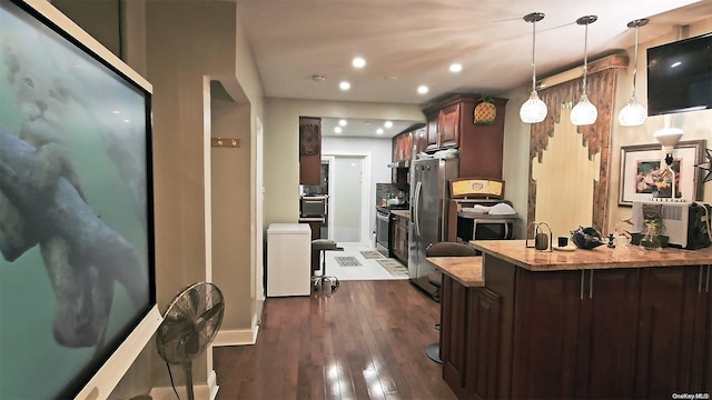 kitchen featuring dark hardwood / wood-style floors, appliances with stainless steel finishes, decorative light fixtures, a kitchen bar, and kitchen peninsula