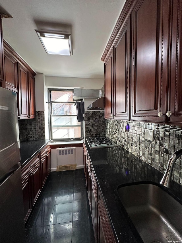 kitchen featuring white gas stovetop, sink, decorative backsplash, stainless steel fridge, and radiator heating unit