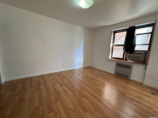 empty room featuring radiator heating unit, cooling unit, and wood-type flooring