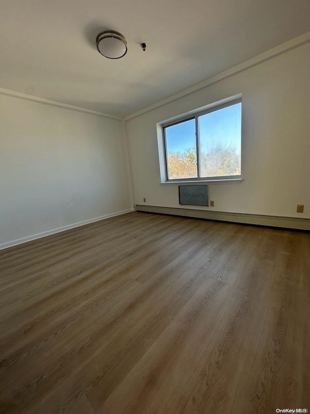 empty room featuring crown molding, wood-type flooring, and a baseboard radiator