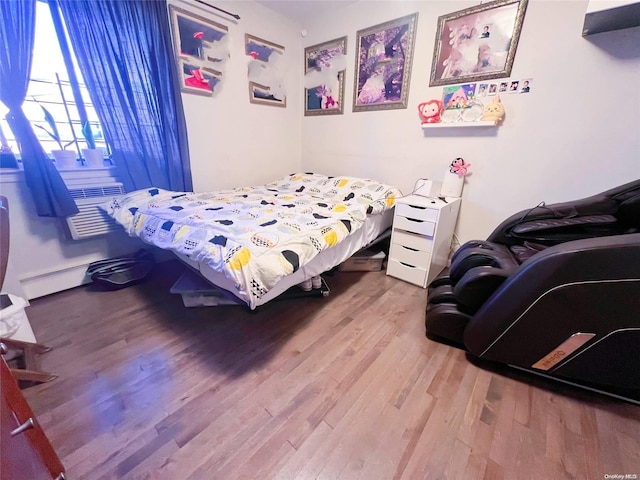 bedroom with an AC wall unit, a baseboard heating unit, and hardwood / wood-style flooring