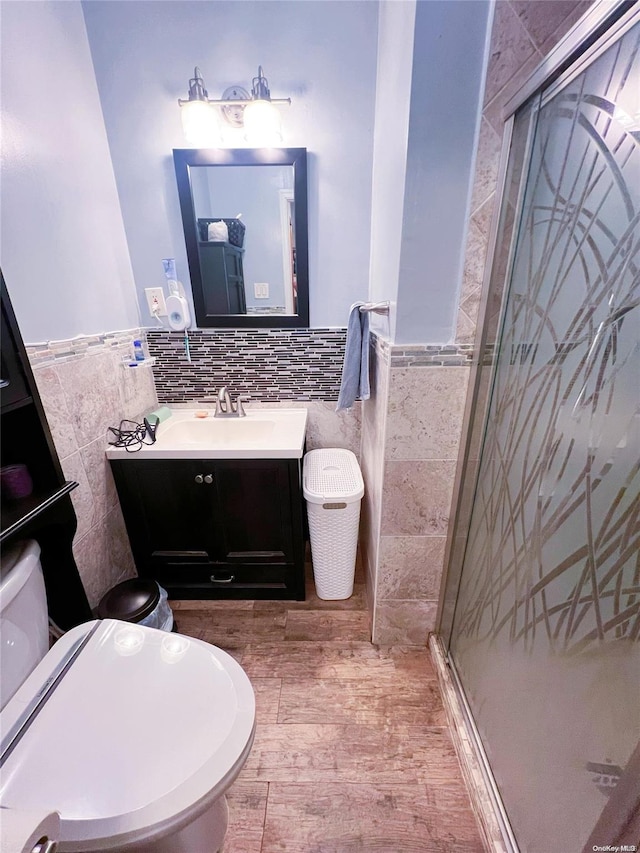 bathroom with wood-type flooring, toilet, a shower with door, vanity, and tile walls