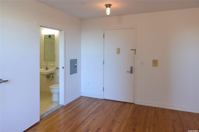 unfurnished bedroom featuring electric panel, ensuite bathroom, and hardwood / wood-style floors