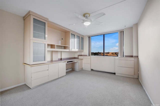 unfurnished office featuring ceiling fan, light colored carpet, and built in desk