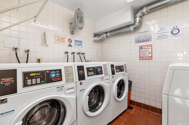 clothes washing area featuring dark tile patterned flooring, washer and clothes dryer, and tile walls