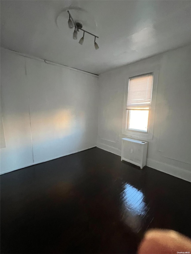 unfurnished room with dark hardwood / wood-style flooring, rail lighting, and radiator