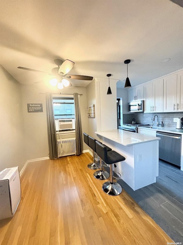 kitchen featuring white cabinetry, radiator heating unit, decorative light fixtures, appliances with stainless steel finishes, and light wood-type flooring