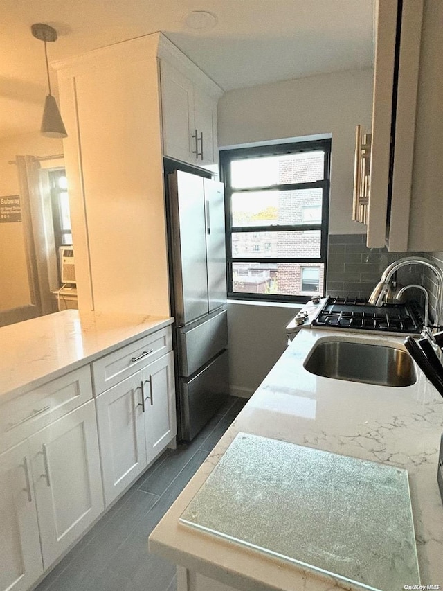 kitchen with decorative backsplash, light stone counters, sink, white cabinets, and stainless steel refrigerator