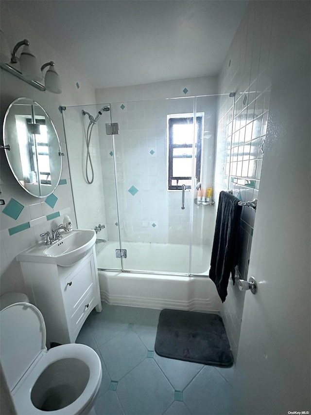 full bathroom featuring combined bath / shower with glass door, tile patterned floors, toilet, vanity, and tile walls