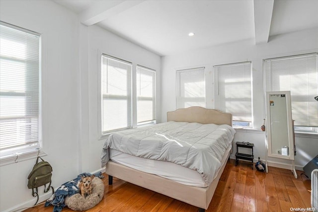 bedroom featuring beamed ceiling, hardwood / wood-style flooring, and multiple windows