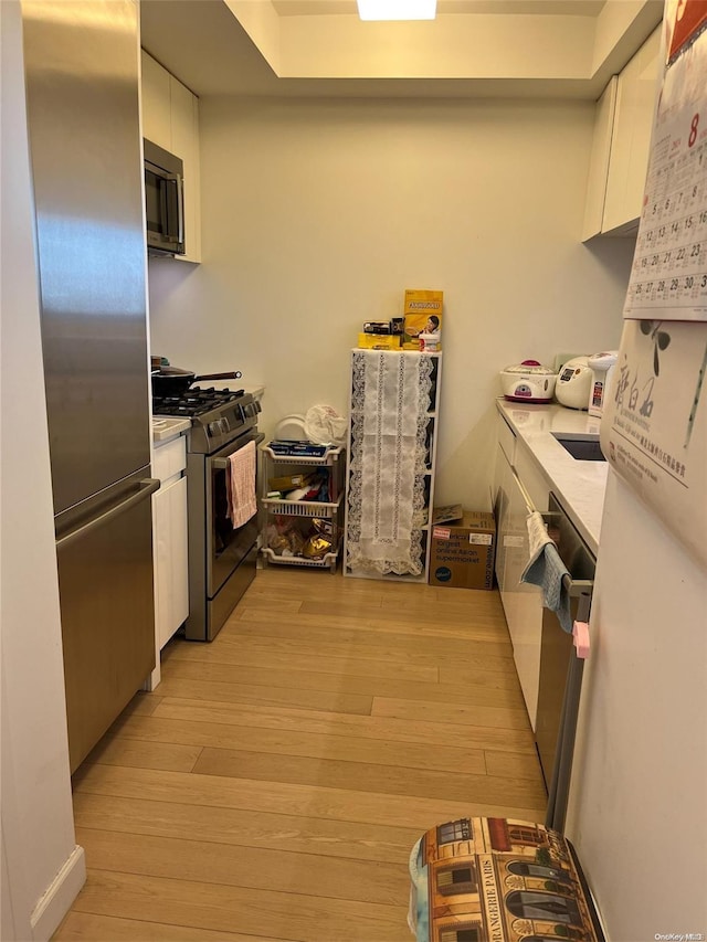 kitchen with light wood-type flooring, stainless steel appliances, and white cabinetry