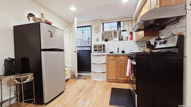 kitchen featuring a baseboard heating unit, decorative backsplash, stainless steel fridge, light wood-type flooring, and black / electric stove