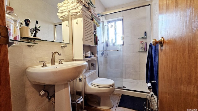 bathroom featuring tile patterned flooring, toilet, a shower with shower door, and tile walls