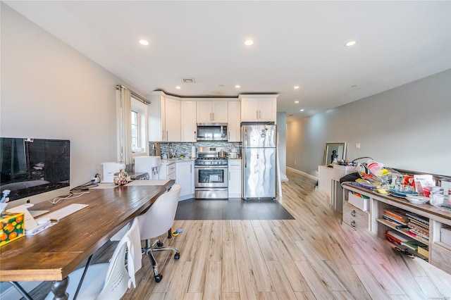 kitchen with appliances with stainless steel finishes, backsplash, light hardwood / wood-style floors, and white cabinetry