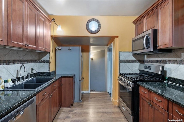 kitchen with sink, stainless steel appliances, dark stone countertops, light hardwood / wood-style floors, and decorative backsplash