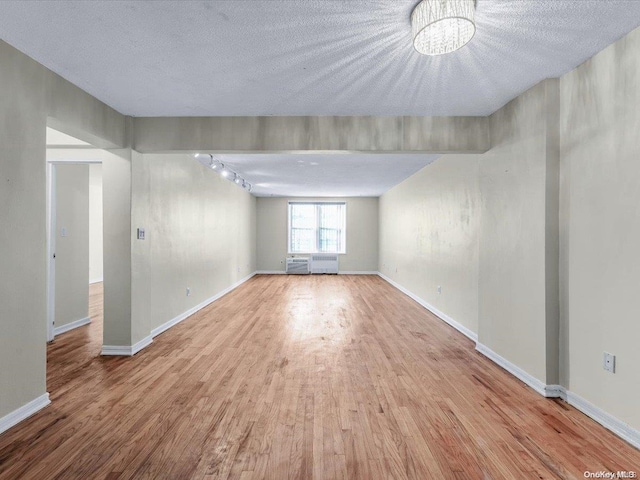 unfurnished room featuring radiator, rail lighting, light hardwood / wood-style flooring, a chandelier, and a textured ceiling