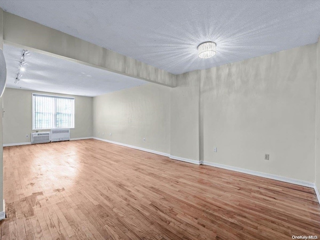 unfurnished room with wood-type flooring, a textured ceiling, rail lighting, and radiator