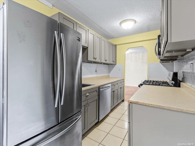 kitchen featuring appliances with stainless steel finishes, backsplash, a textured ceiling, gray cabinets, and light tile patterned flooring