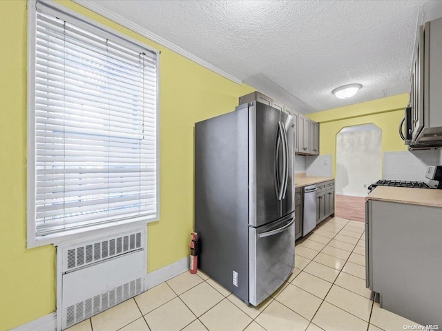 kitchen with a wealth of natural light, radiator heating unit, light tile patterned floors, and stainless steel appliances