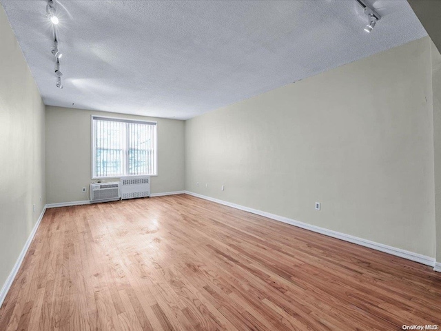 empty room with a textured ceiling, radiator heating unit, rail lighting, and light hardwood / wood-style flooring