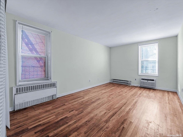 unfurnished room featuring hardwood / wood-style flooring, a wall unit AC, radiator, and a baseboard radiator