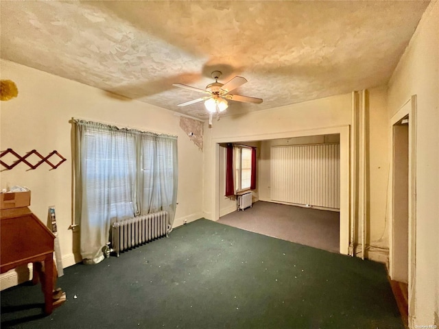 unfurnished bedroom featuring ceiling fan, dark carpet, and radiator heating unit