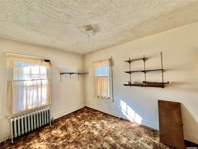 empty room with radiator heating unit, a textured ceiling, and dark colored carpet