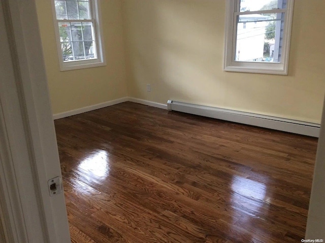 unfurnished room featuring a wealth of natural light, baseboard heating, and dark wood-type flooring