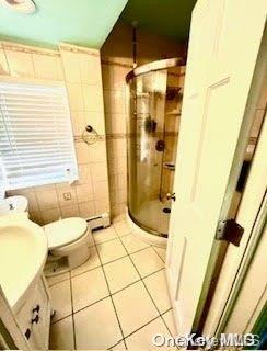 bathroom featuring tile patterned flooring, toilet, vanity, a shower with shower door, and tile walls