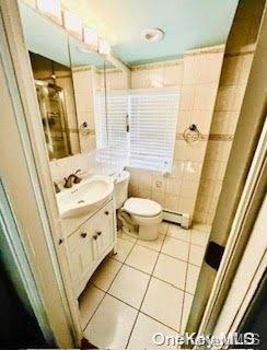 bathroom featuring baseboard heating, tile patterned flooring, toilet, vanity, and tile walls