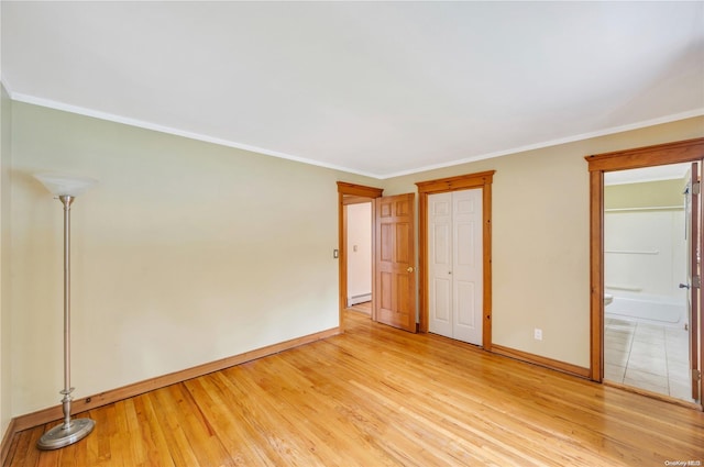 unfurnished bedroom with baseboard heating, ensuite bathroom, ornamental molding, and light wood-type flooring