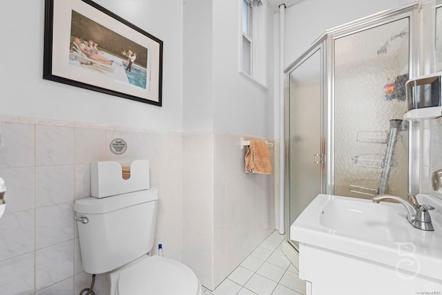 bathroom with tile patterned floors, toilet, a shower with door, vanity, and tile walls