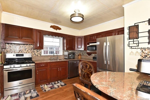 kitchen with light stone countertops, sink, stainless steel appliances, backsplash, and hardwood / wood-style floors