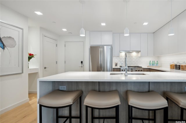 kitchen featuring stainless steel fridge, backsplash, light hardwood / wood-style flooring, white cabinets, and a breakfast bar area