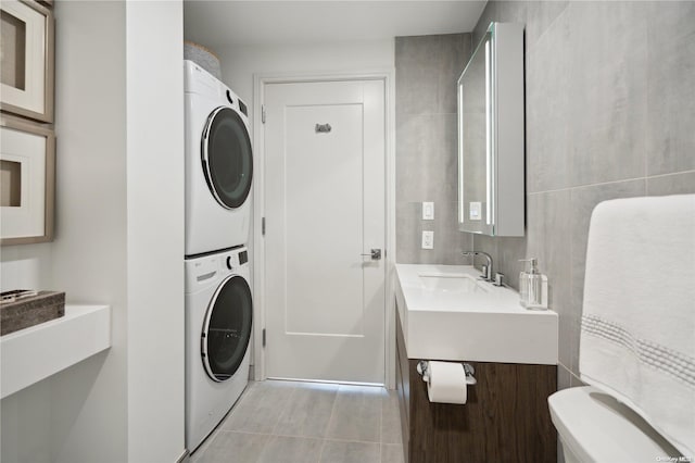 laundry area featuring light tile patterned floors, tile walls, stacked washer / drying machine, and sink