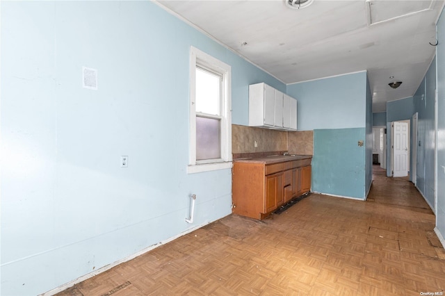 kitchen with sink, light parquet flooring, white cabinetry, and backsplash