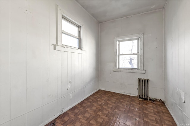 unfurnished room featuring wood walls, dark parquet flooring, and radiator