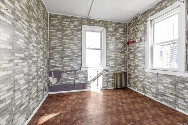 empty room featuring a wealth of natural light, dark parquet flooring, and radiator