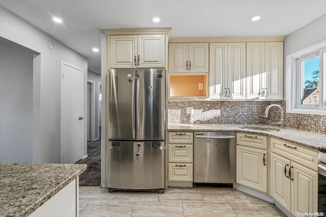 kitchen featuring cream cabinets, sink, decorative backsplash, appliances with stainless steel finishes, and light stone counters