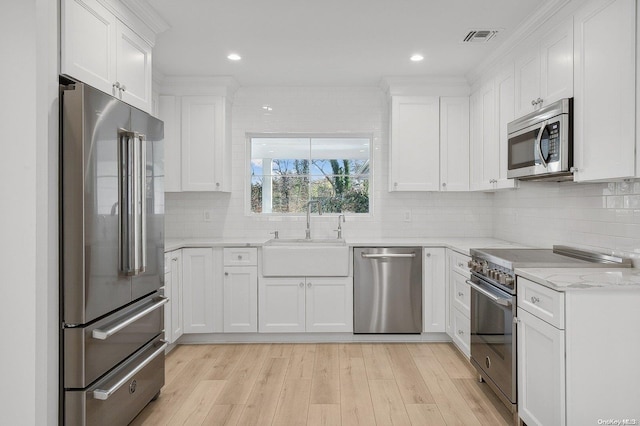 kitchen featuring high quality appliances, white cabinetry, sink, and light hardwood / wood-style flooring