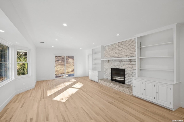 unfurnished living room with built in features, light wood-type flooring, and a brick fireplace