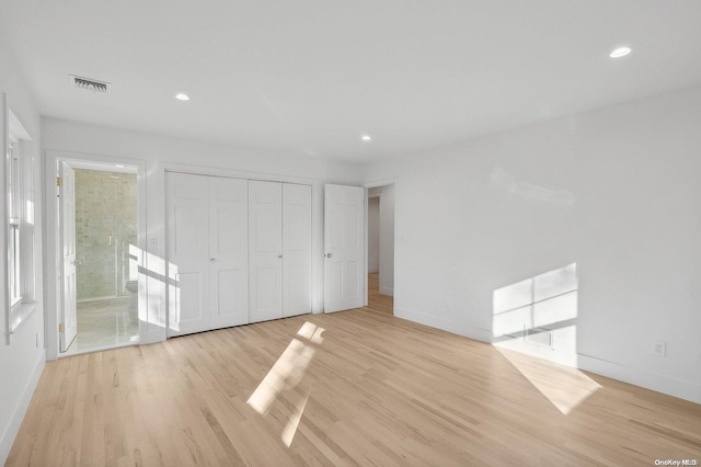 unfurnished bedroom featuring ensuite bath, a closet, and light wood-type flooring