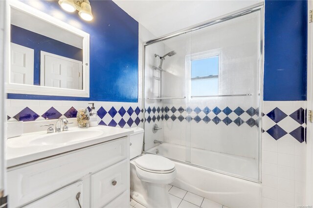 full bathroom with combined bath / shower with glass door, vanity, tile walls, tile patterned flooring, and toilet