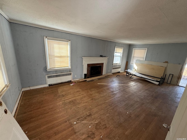 unfurnished living room featuring radiator, hardwood / wood-style floors, a textured ceiling, and a brick fireplace