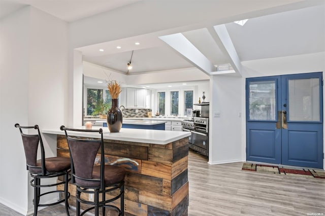 kitchen featuring stainless steel appliances, light hardwood / wood-style flooring, kitchen peninsula, decorative backsplash, and white cabinets