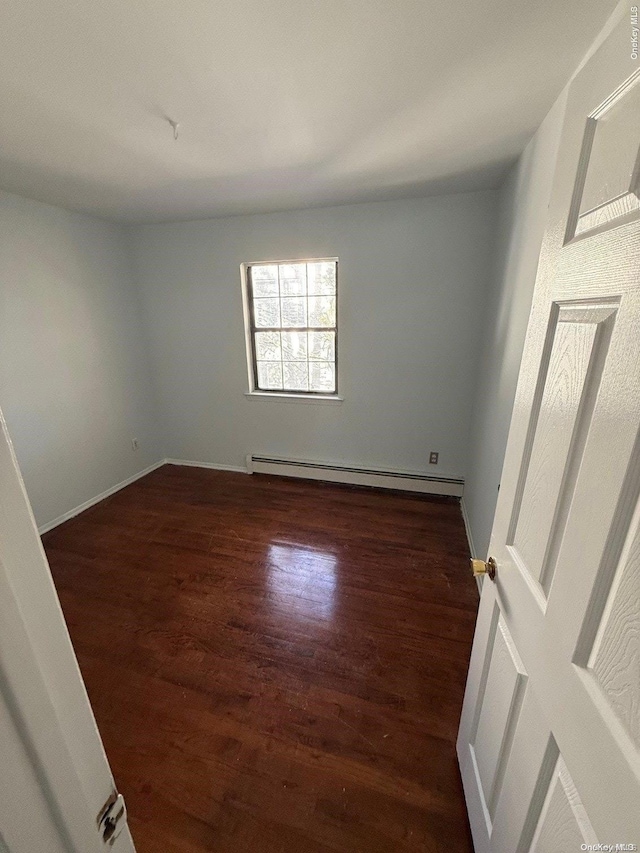 empty room with baseboard heating and dark hardwood / wood-style flooring