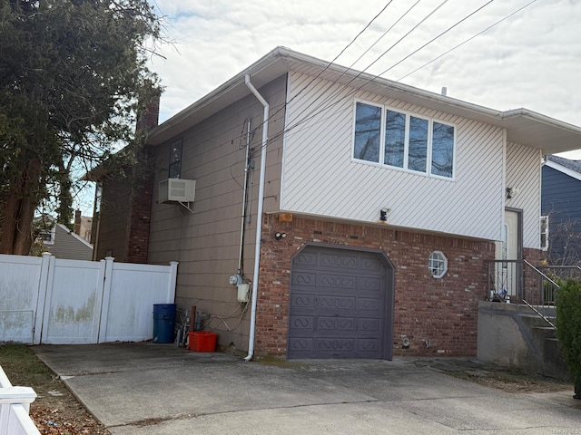 view of property exterior with brick siding, fence, a garage, and driveway